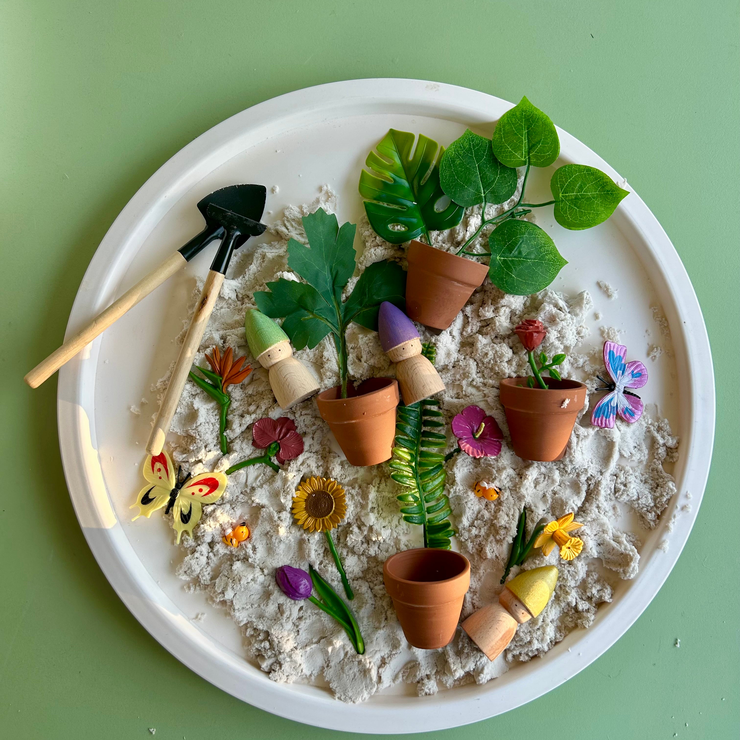 Playful arrangement of small plants, pots, and gardening tools on a white plate with a green background