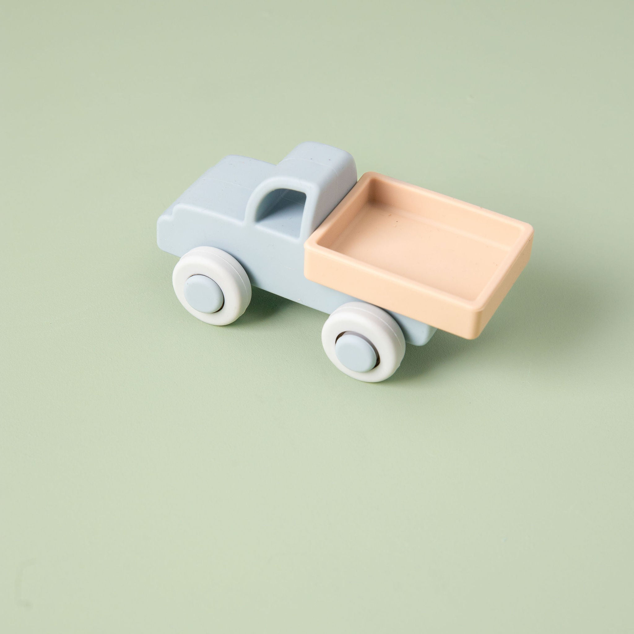 Silicone toy truck with a light blue body and pink bed on a green background