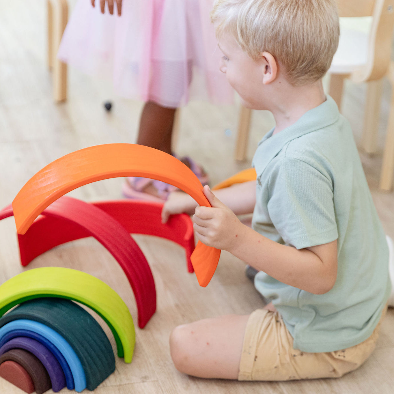 Child playing with rainbow stacker arches on a play mat — open-ended Montessori building