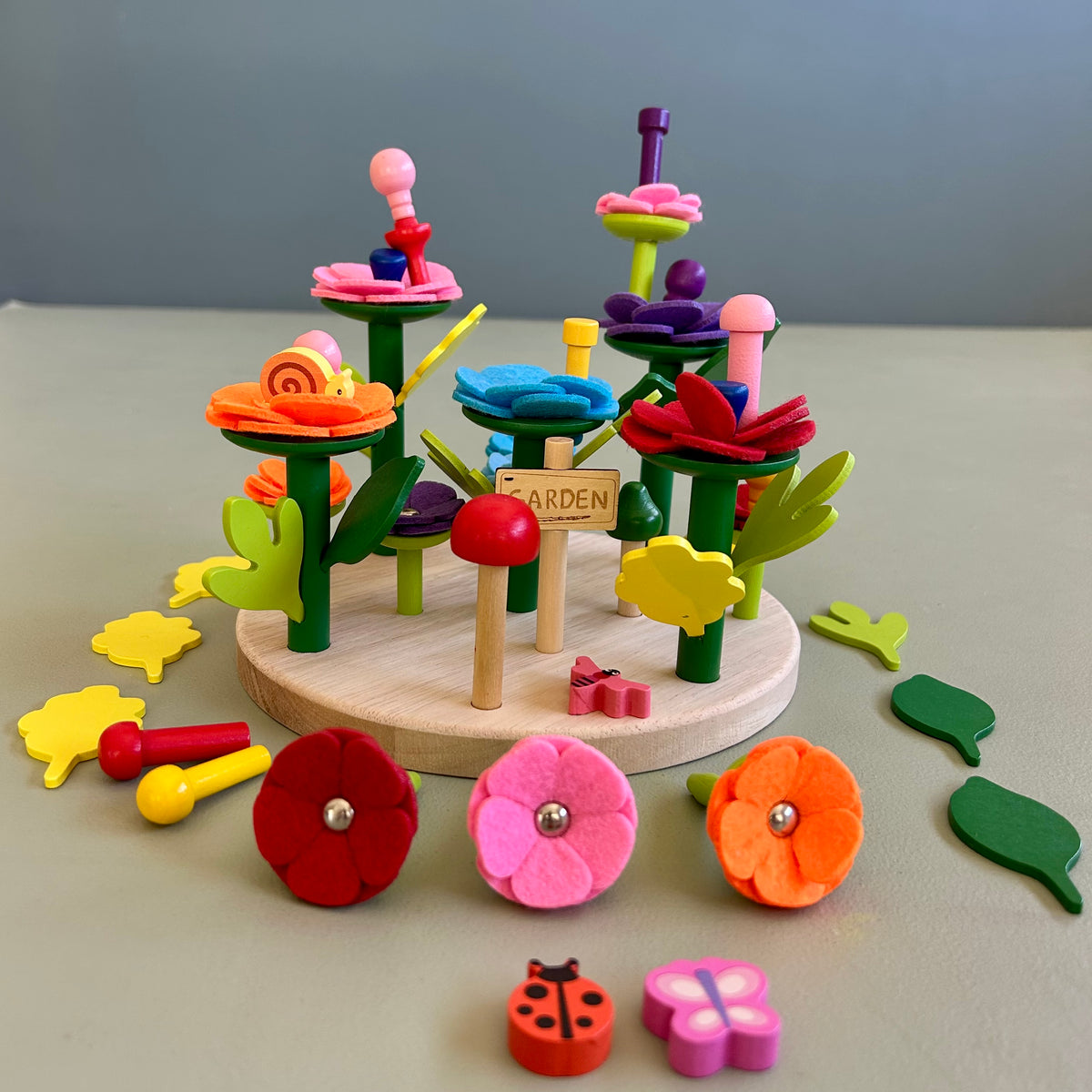 A wooden baseboard game featuring colorful felt leaves, flowers, a tree, and animal figures.