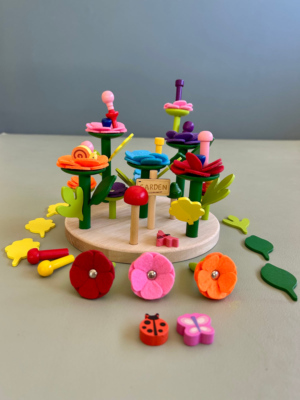 A wooden baseboard game featuring colorful felt leaves, flowers, a tree, and animal figures.