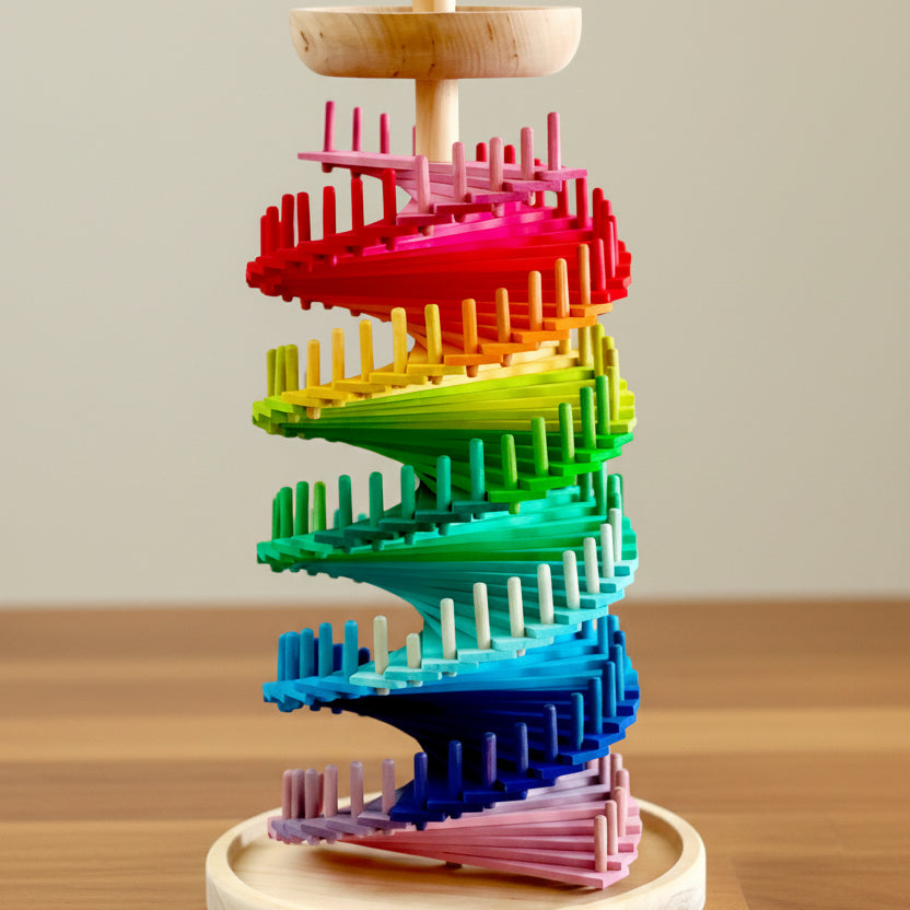 Tall wooden marble tower with rainbow-coloured discs spiralling around a central post on a round wooden base, shown with a set of wooden balls beside it and dimension markers indicating height and base width