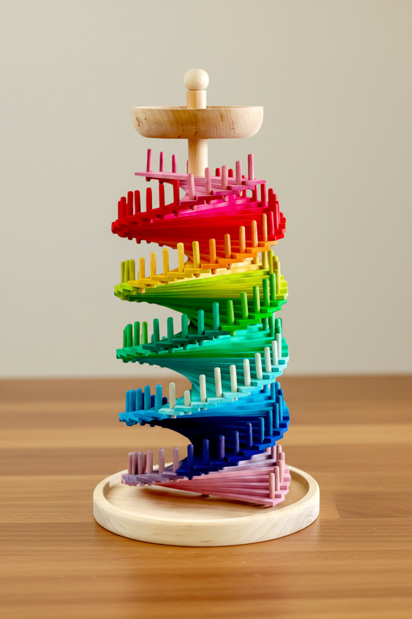 Tall wooden marble tower with rainbow-coloured discs spiralling around a central post on a round wooden base, shown with a set of wooden balls beside it and dimension markers indicating height and base width