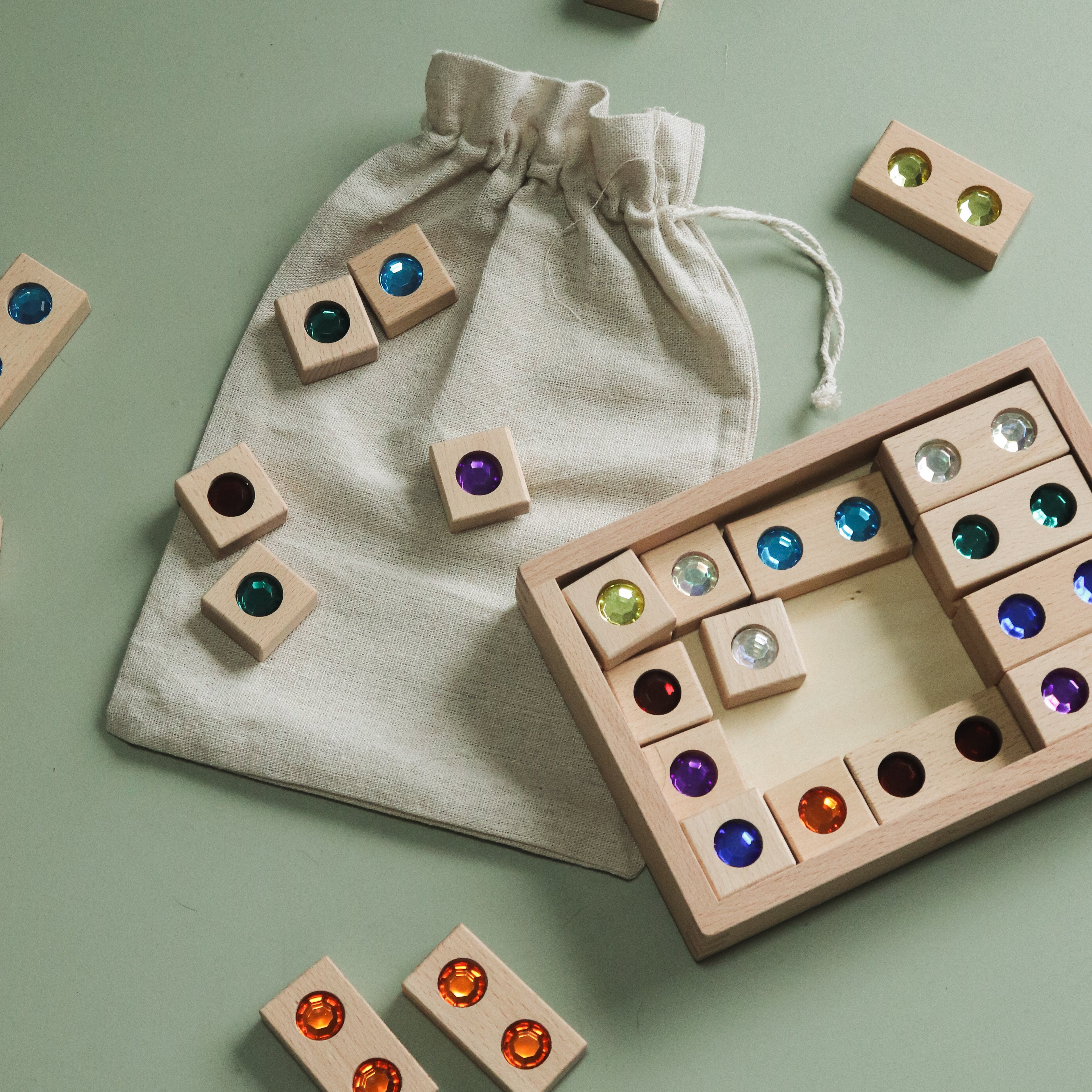 Wooden gem blocks arranged next to the wooden storage box and drawstring bag to show relative piece size and set packaging.