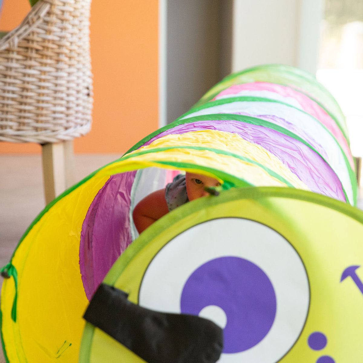 Toddler crawling on hands and knees through a pop-up play tunnel on a soft rug at home
