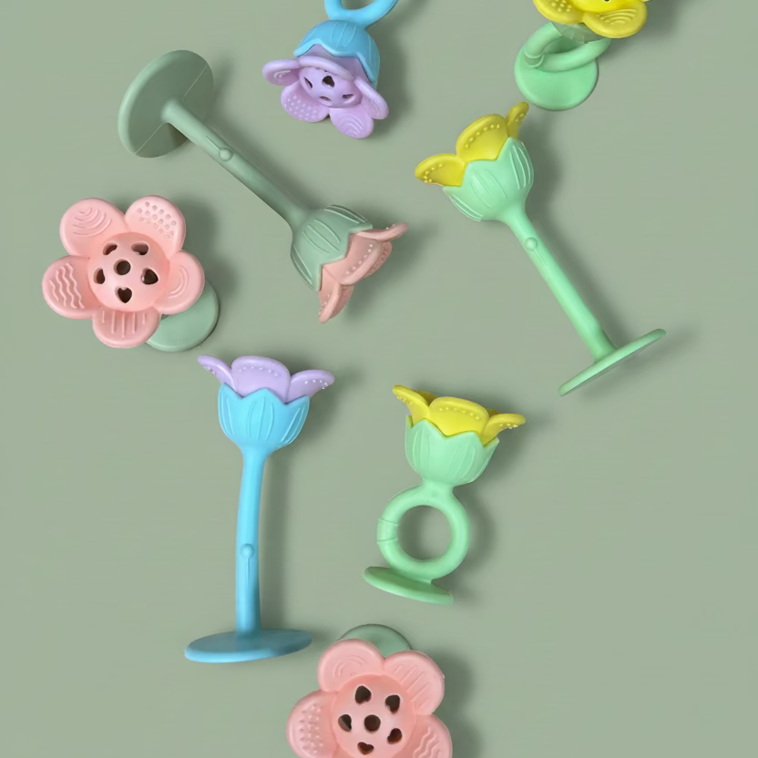 A set of colorful baby teething toys with flower and mushroom designs, arranged on a light brown wooden surface.