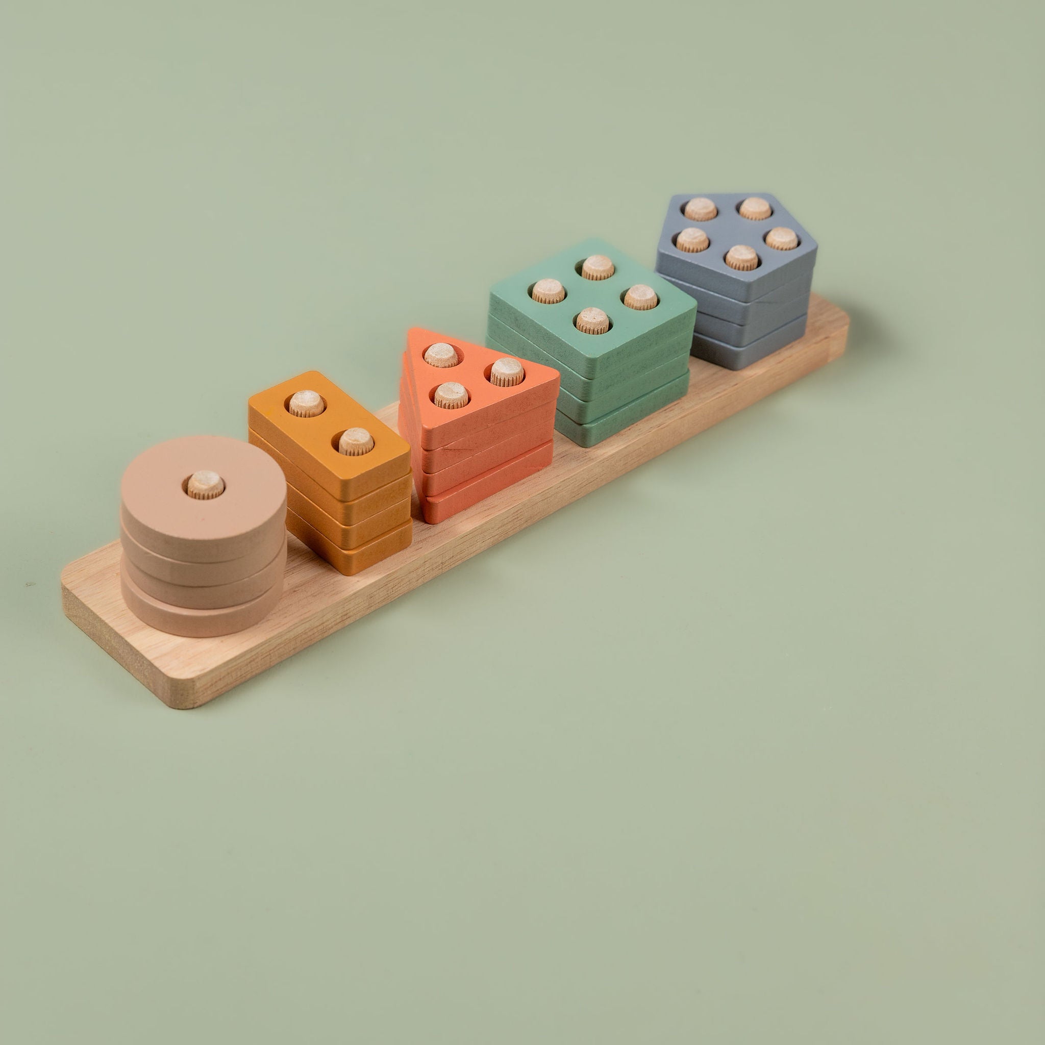Close-up of pastel geometric shape sorter showing circle, triangle, square, rectangle and pentagon pieces in soft colours