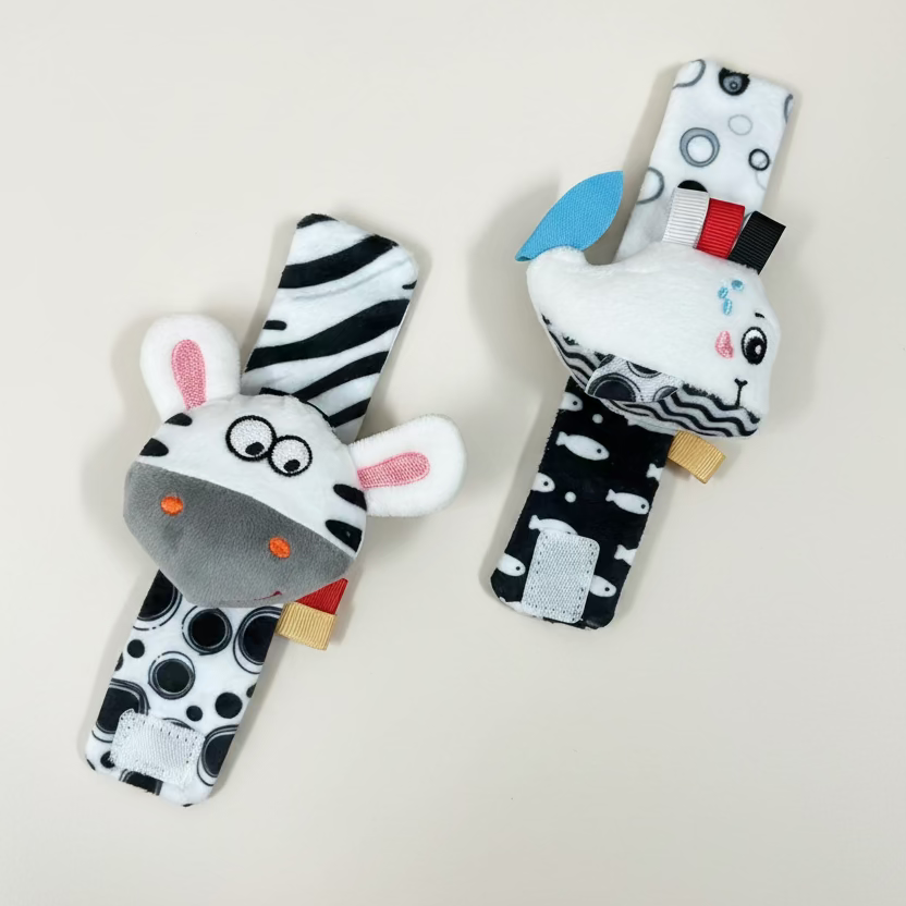 Two plush baby rattle toys shaped like zebra heads, displayed on a liOne rattle features black and white stripes with pink inner ears and a gray snout. wrist rattle high contrast