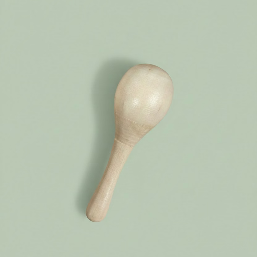 A small handcrafted wooden maraca or shaker with a smooth, rounded head and a tapered handle, resting on a light-colored wooden surface.