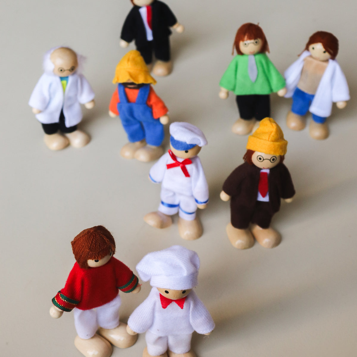 A set of nine wooden dolls representing various occupations, including a scientist, doctor, engineer, sailor, business man, chef, farmer, athlete, and teacher, each dressed in attire appropriate to their profession.