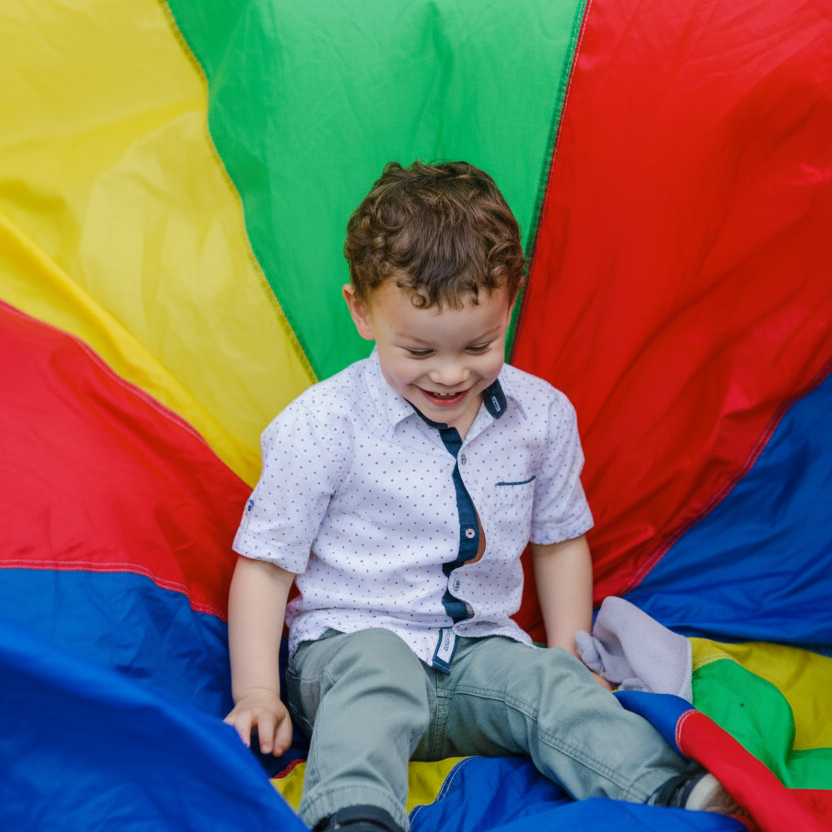 boy sitting on big colourful parachute- gross motor play