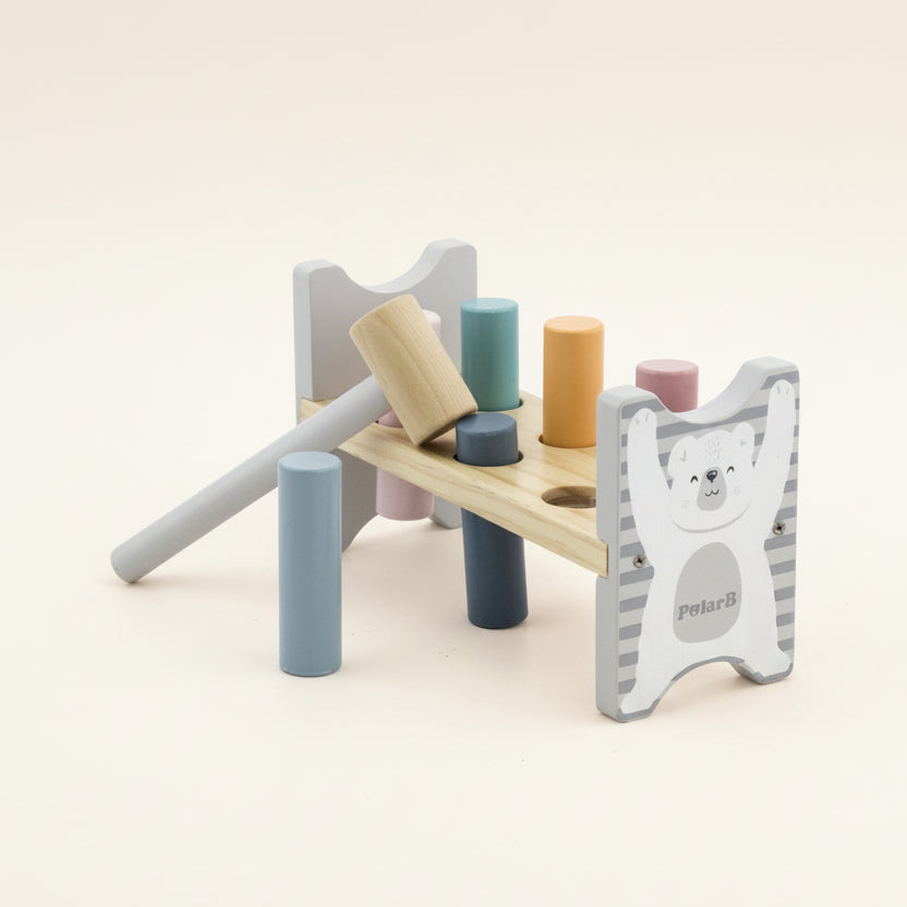 A wooden toy block hammer set by PolarB, featuring a light natural wood mallet, colorful wooden pegs in blue, teal, orange, pink, and navy, and a white bear-themed guard with gray stripes.