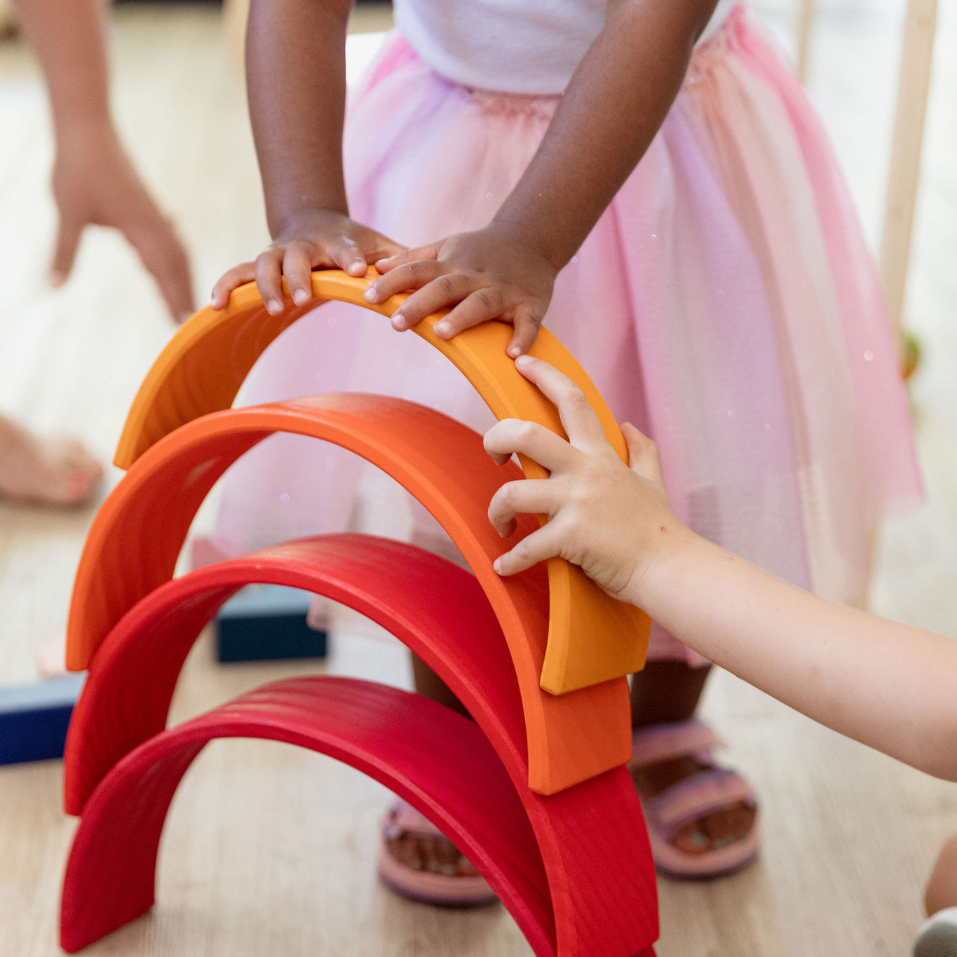 Toddler hands placing a wooden arch onto a rainbow stacker tower — fine motor play