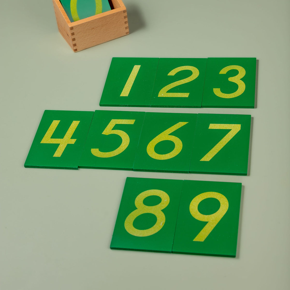 A set of ten sandpaper numeral boards (0–9) arranged together, each showing a textured numeral mounted on a green board, presented alongside their wooden storage box.