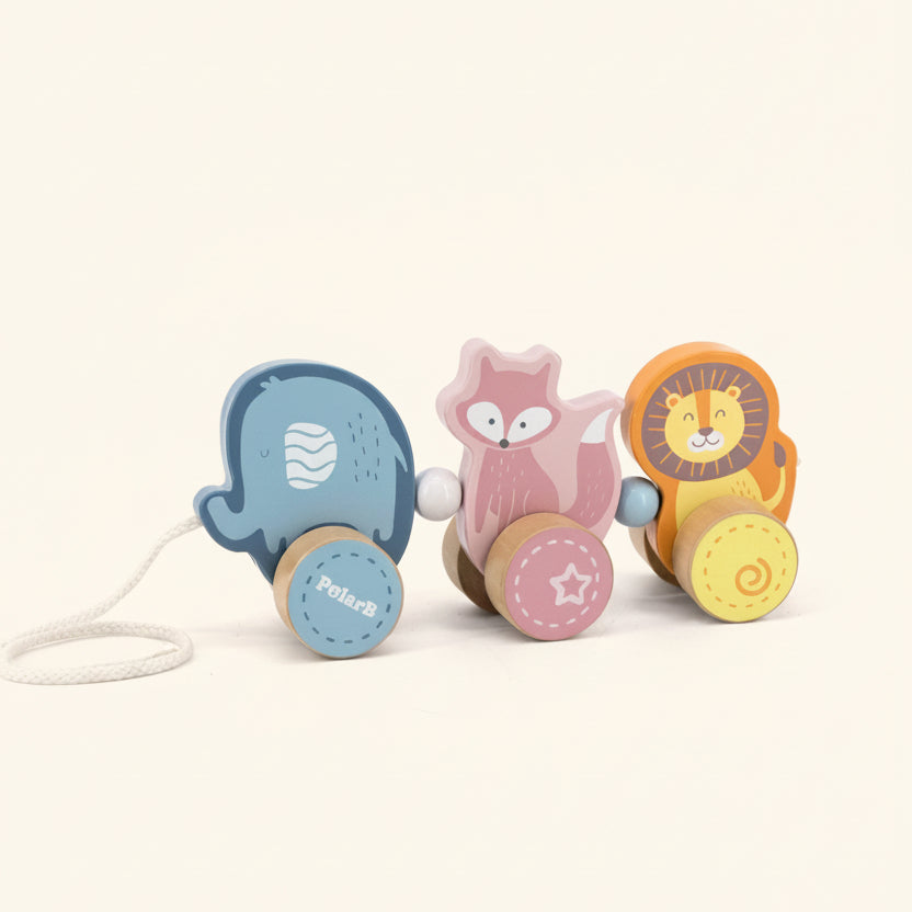 A wooden toy train set with three animal characters: a blue polar bear, a pink fox, and an orange lion, each with a round wooden wheel. The toy is photographed on a clean white background.