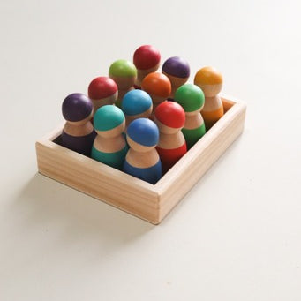 A set of colorful wooden peg dolls placed in a wooden tray, with no facial features painted on the dolls.