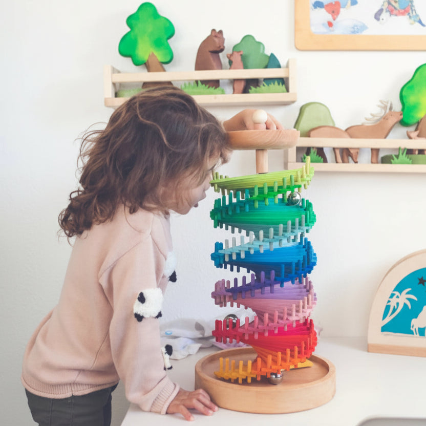 Child dropping a wooden marble into the top of the rainbow marble tower