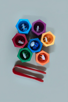 A set of colorful plastic bird feeder cups in blue, purple, red, orange, green, and dark blue, each containing bird seed, accompanied by a red scoop, arranged on a light blue  background.