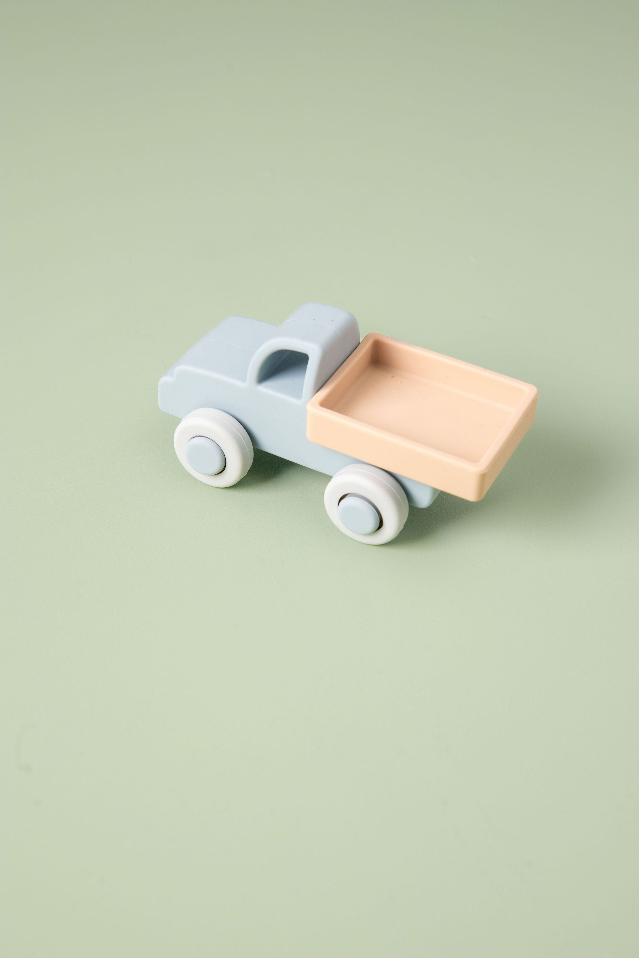Silicone toy truck with a light blue body and pink bed on a green background