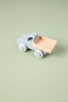 Silicone toy truck with a light blue body and pink bed on a green background