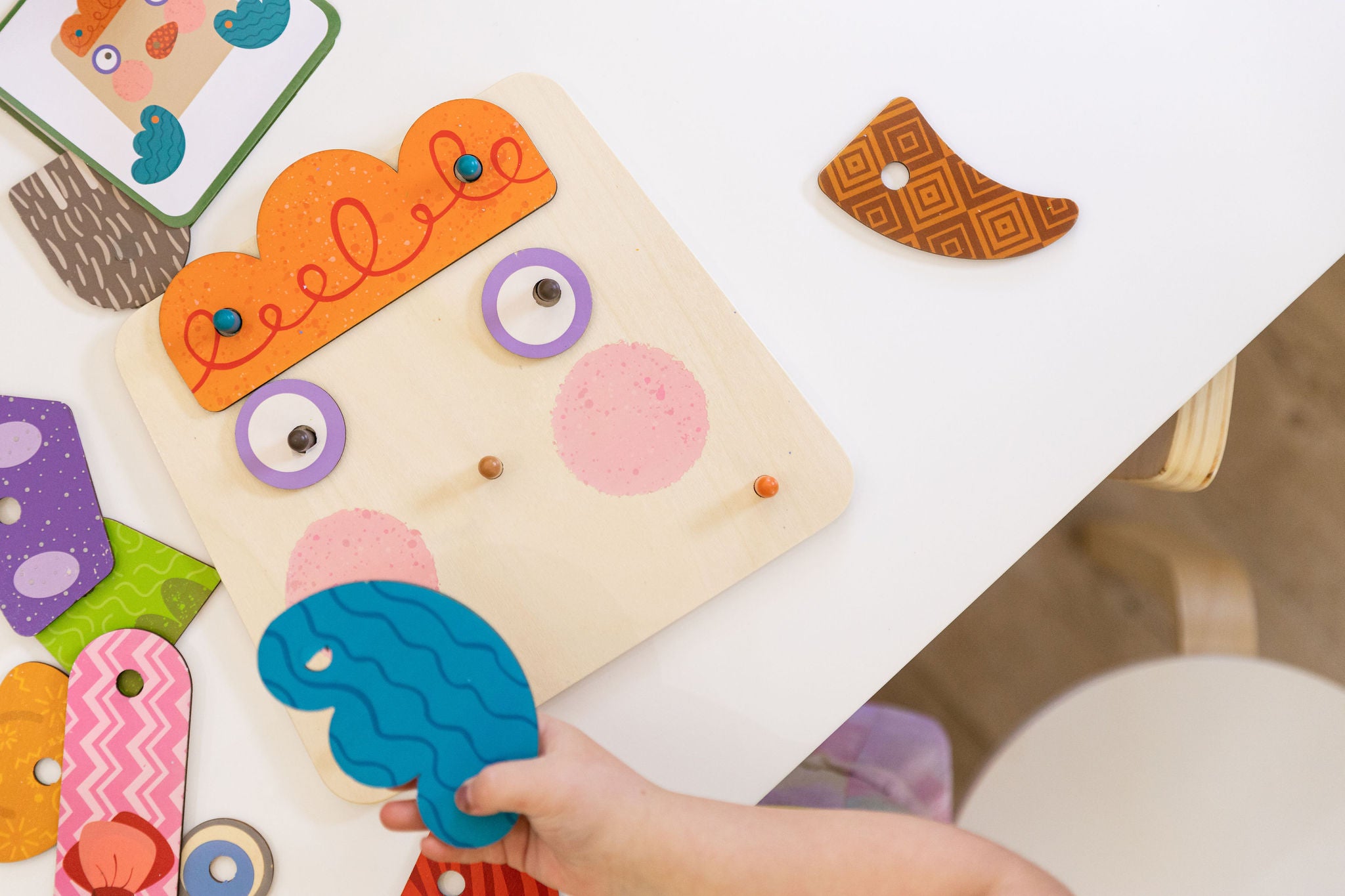 Child playing with a wooden puzzle shaped like a face on a white surface.