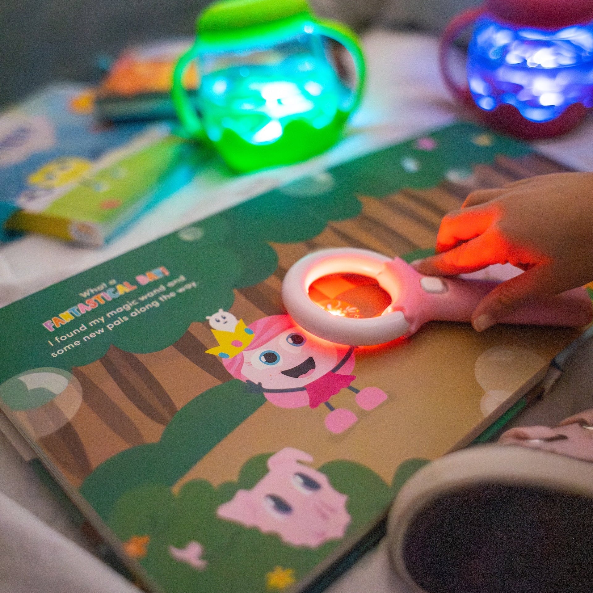 Child's hand holding a light-up toy over a children's book with colorful background