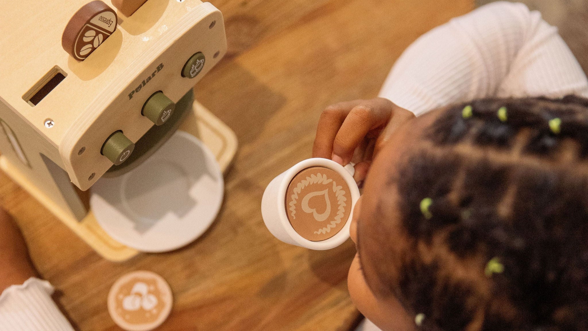 Child playing with a toy coffee machine and cup on a wooden table