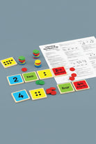 Learning Numbers 1-10 educational game set with colorful square tiles showing numbers and words, green and red circular tokens, and printed worksheet pages on a white background.