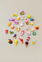 A collection of various mini erasers in different shapes and colors arranged on a grey surface.
