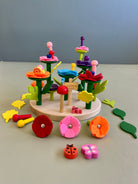 A wooden baseboard game featuring colorful felt leaves, flowers, a tree, and animal figures.
