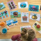 Children's playdough activity cards on a wooden table with a child interacting with them.