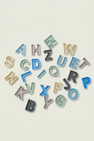 A collection of colorful alphabet letter cutouts in various shades of blue, green, beige, and white, scattered on a plain light beige surface.
