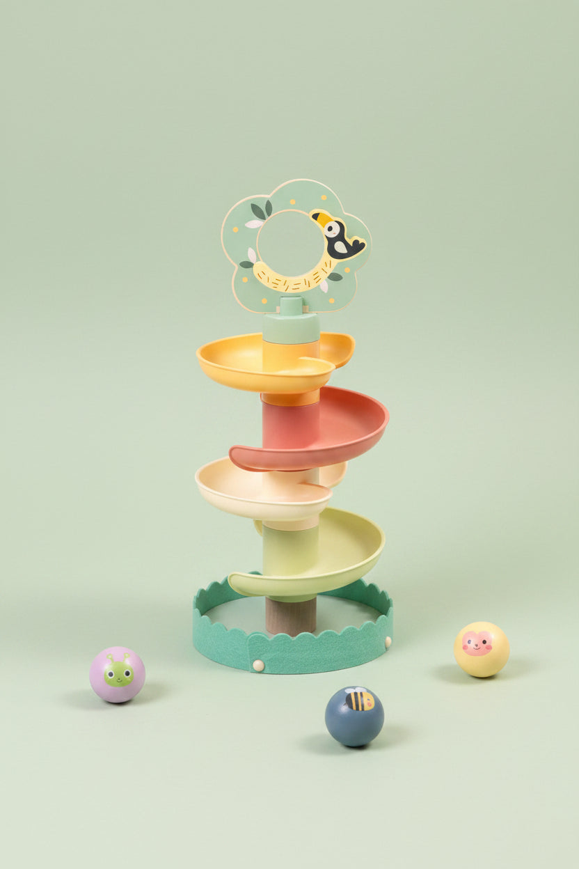 A pastel spiral toy with four winding levels in mint green, yellow, peach, and cream, topped with a flower-shaped ring holder. Small painted balls are placed around it on a light beige textured surface against a soft cream background.