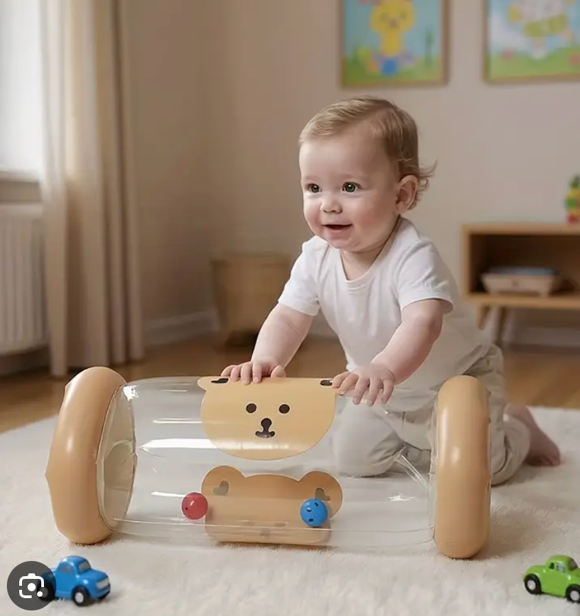 A baby in a white onesie kneels on a white rug playing with a transparent plastic bear-shaped toy walker with tan wheels in a softly lit nursery.