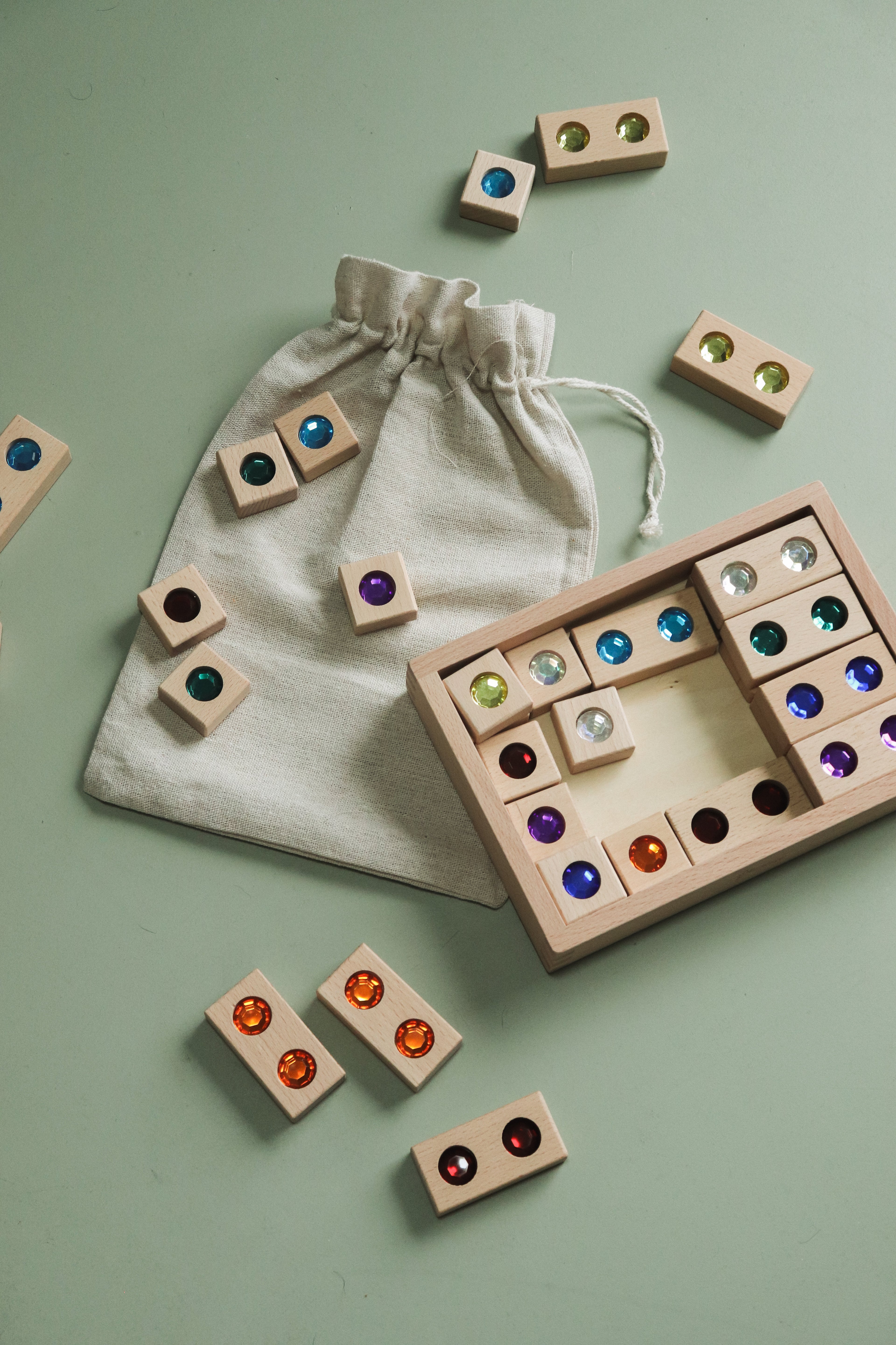 Wooden gem blocks arranged next to the wooden storage box and drawstring bag to show relative piece size and set packaging.