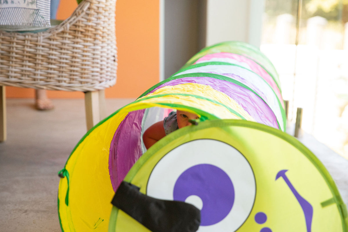 Toddler crawling on hands and knees through a pop-up play tunnel on a soft rug at home
