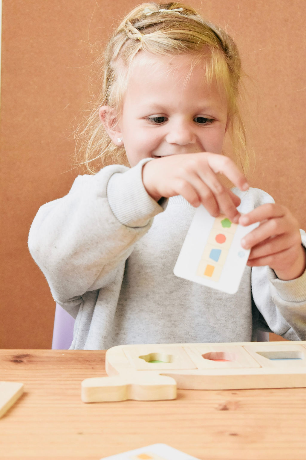 A child’s hands turning a wooden shape block to fit it onto the whale board, with a puzzle card propped up beside them.