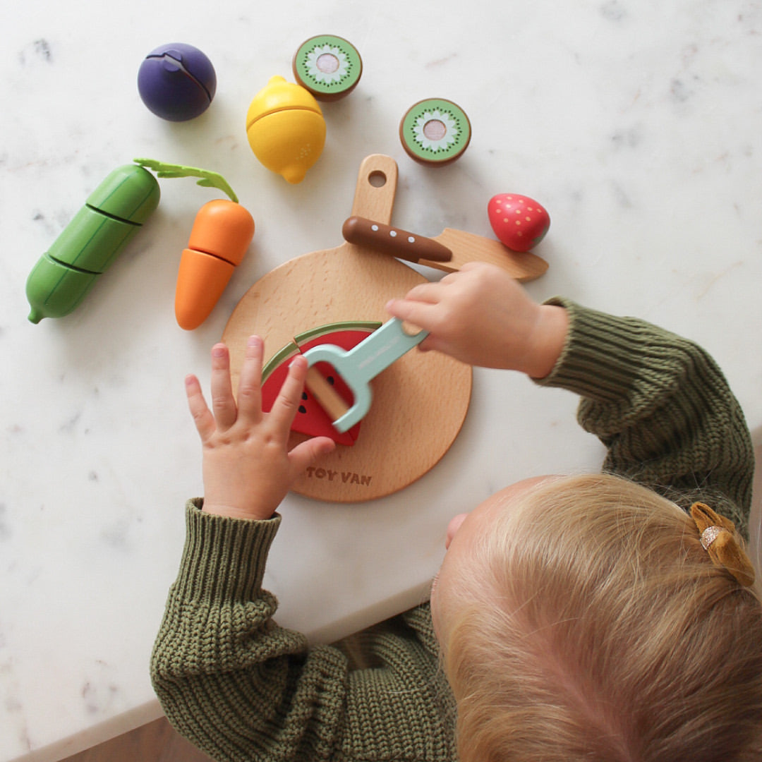 Child playing with toy fruits and vegetables on a marble surface