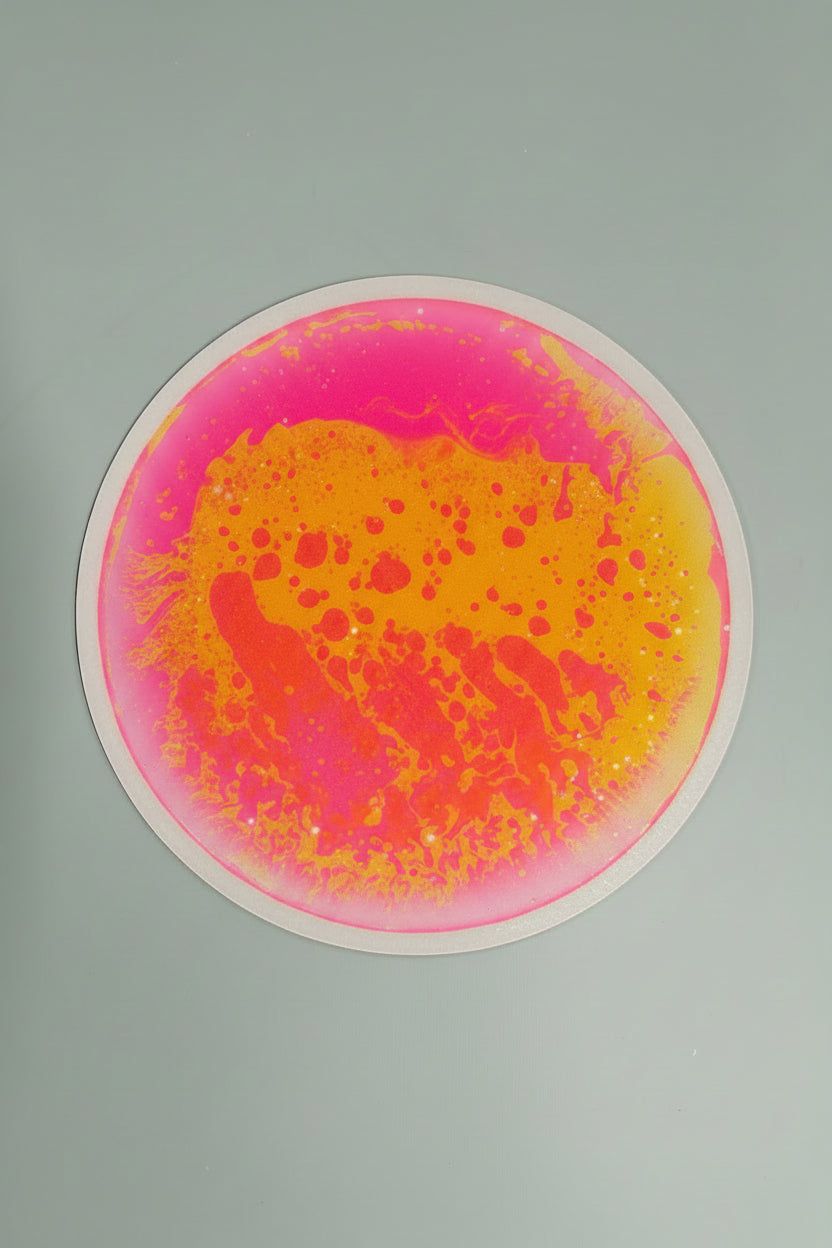 A circular liquid tile  with a vibrant abstract design featuring bright pink and yellow-orange paint splatters on a light gray background.