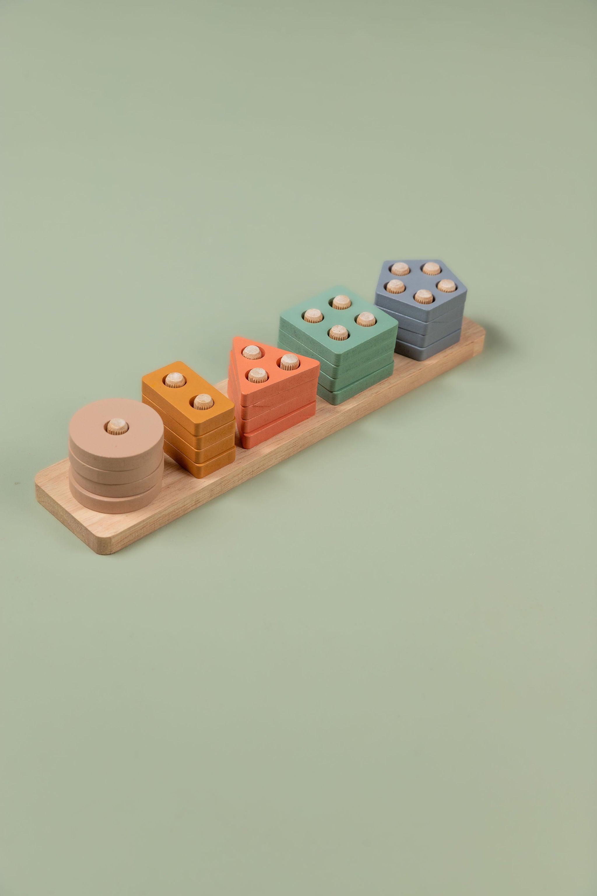 Close-up of pastel geometric shape sorter showing circle, triangle, square, rectangle and pentagon pieces in soft colours