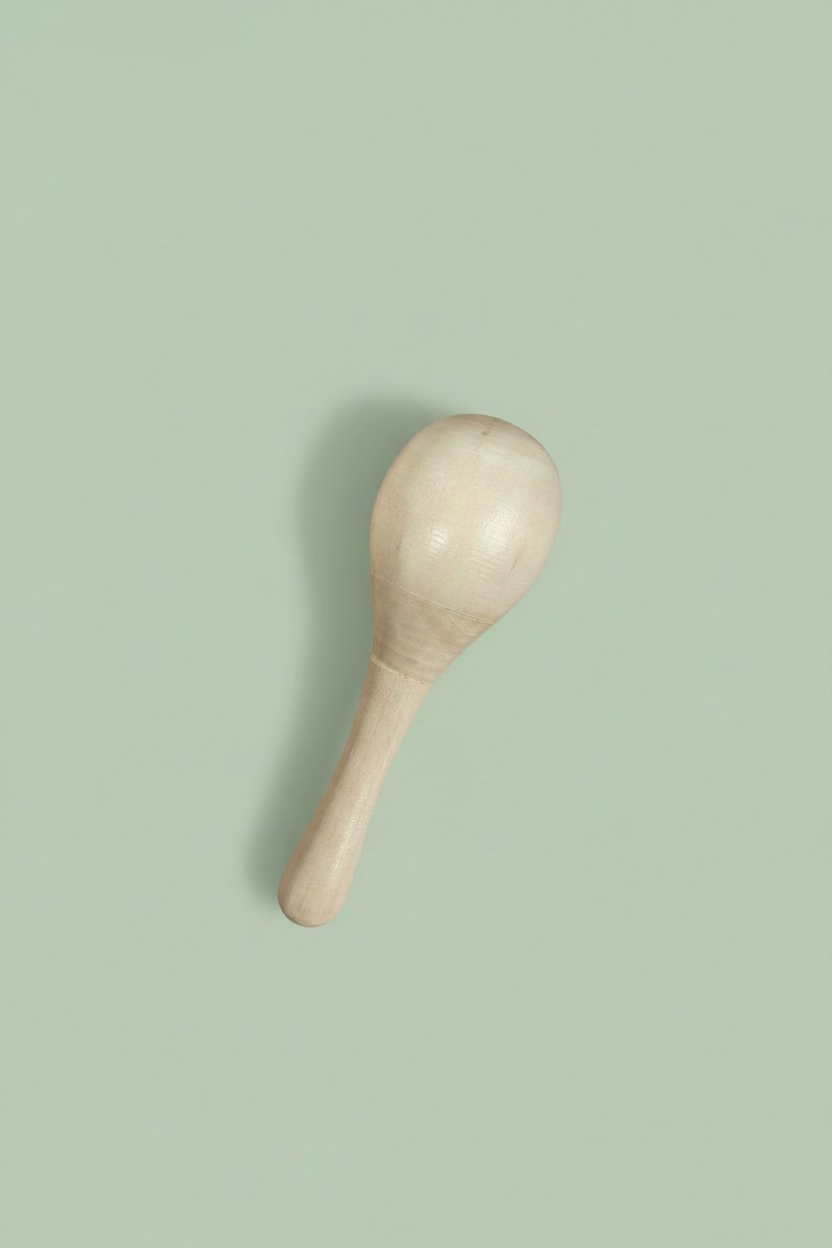 A small handcrafted wooden maraca or shaker with a smooth, rounded head and a tapered handle, resting on a light-colored wooden surface.