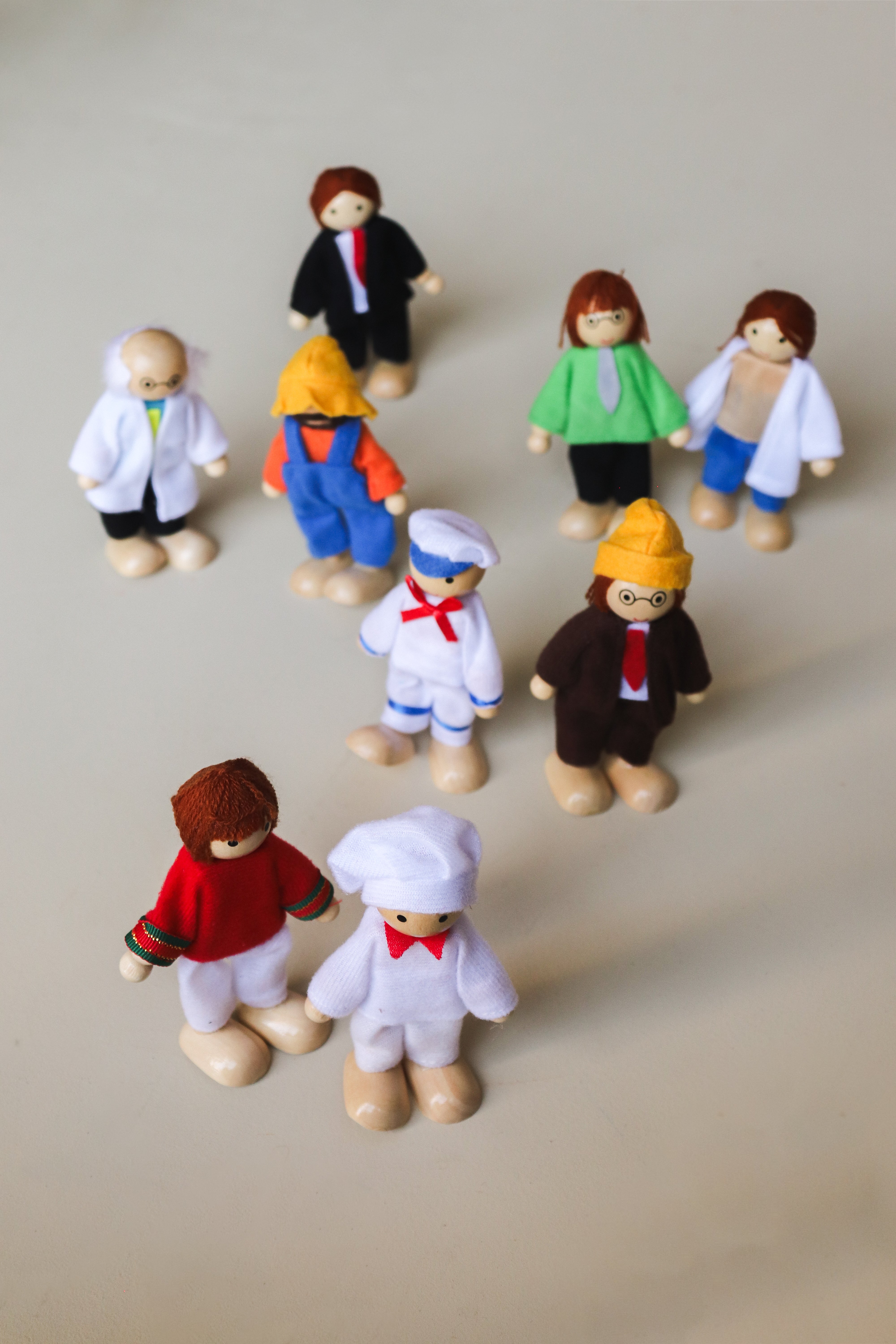 A set of nine wooden dolls representing various occupations, including a scientist, doctor, engineer, sailor, business man, chef, farmer, athlete, and teacher, each dressed in attire appropriate to their profession.