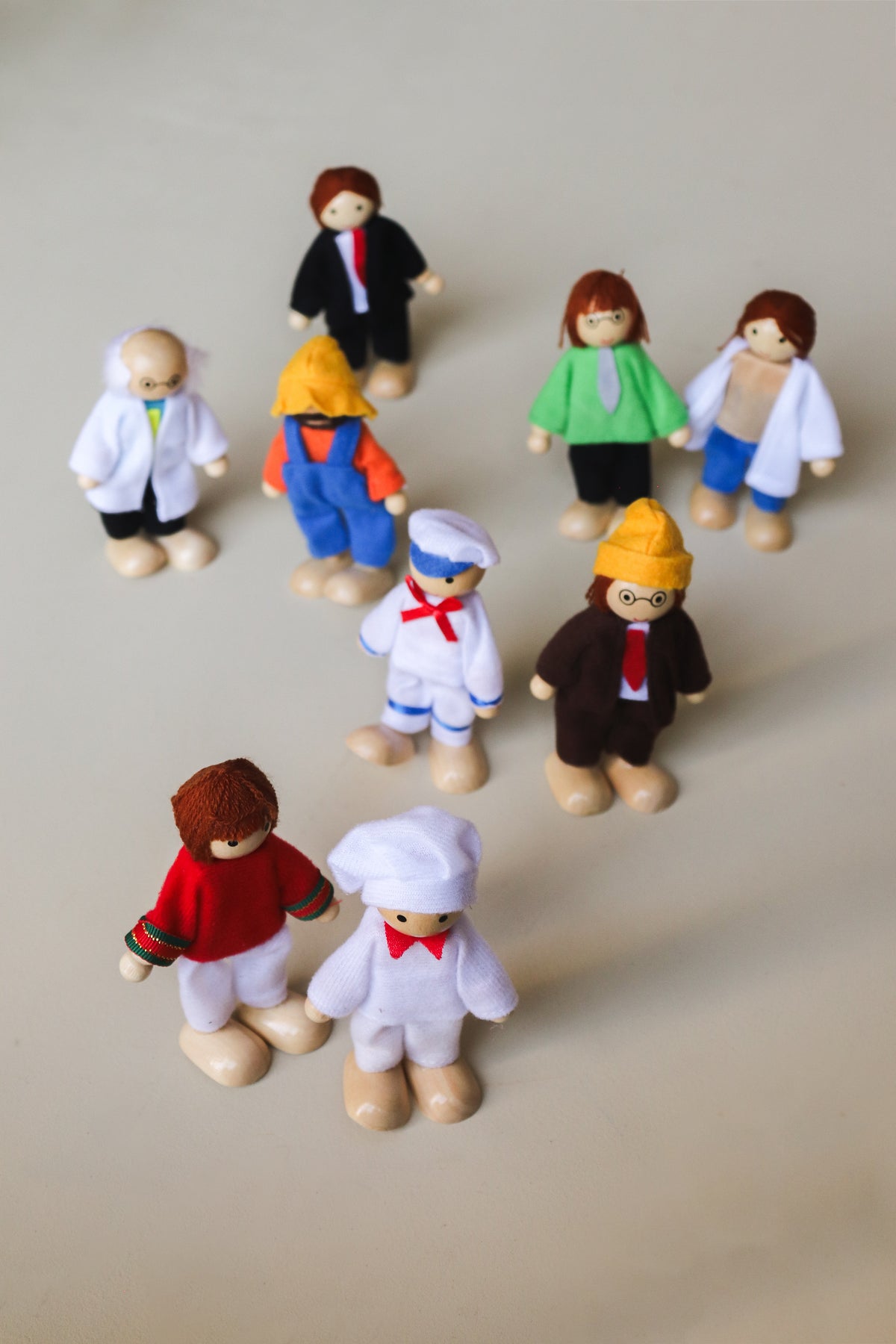 A set of nine wooden dolls representing various occupations, including a scientist, doctor, engineer, sailor, business man, chef, farmer, athlete, and teacher, each dressed in attire appropriate to their profession.