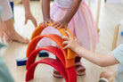 Toddler hands placing a wooden arch onto a rainbow stacker tower — fine motor play