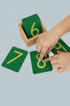 A child tracing a sandpaper numeral with their fingertip, demonstrating the tactile tracing motion.