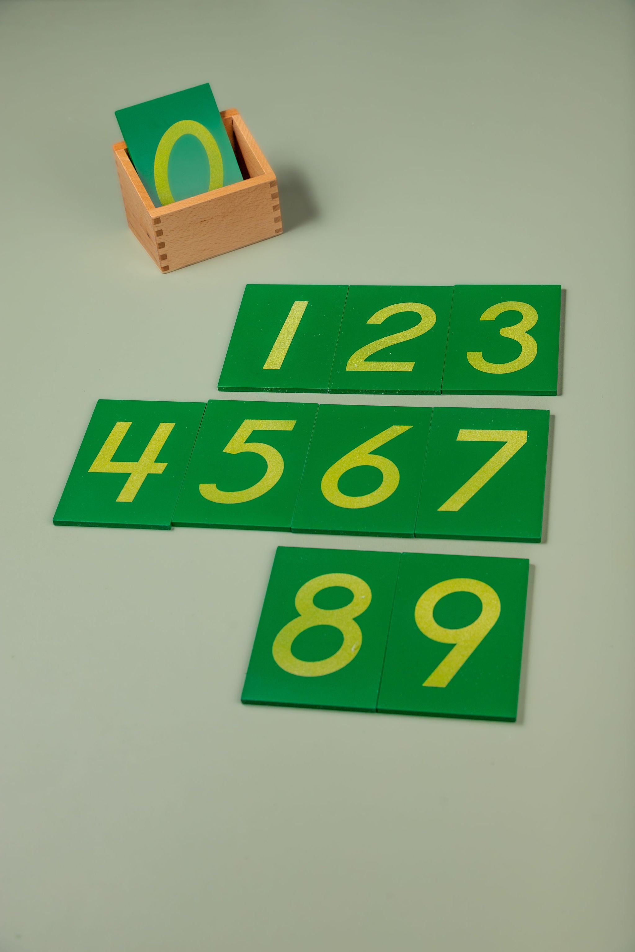 A set of ten sandpaper numeral boards (0–9) arranged together, each showing a textured numeral mounted on a green board, presented alongside their wooden storage box.
