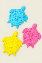 Three turtle-shaped silicone stepping stones  in light blue, bright yellow, and hot pink, arranged on a light wood tabletop.