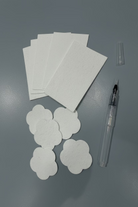 White cloud-shaped sponge shaped paper for painting  arranged next to a clear water brush and a small clear cap on a light gray surface.
