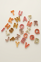 A scattered set of colorful silicone alphabet letters  on a beige  surface.