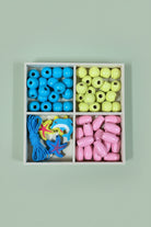A wooden four-compartment box containing colorful craft beads: blue round beads, yellow oval beads, pink teardrop beads, and blue starfish and shark-shaped beads, placed on a wooden surface.